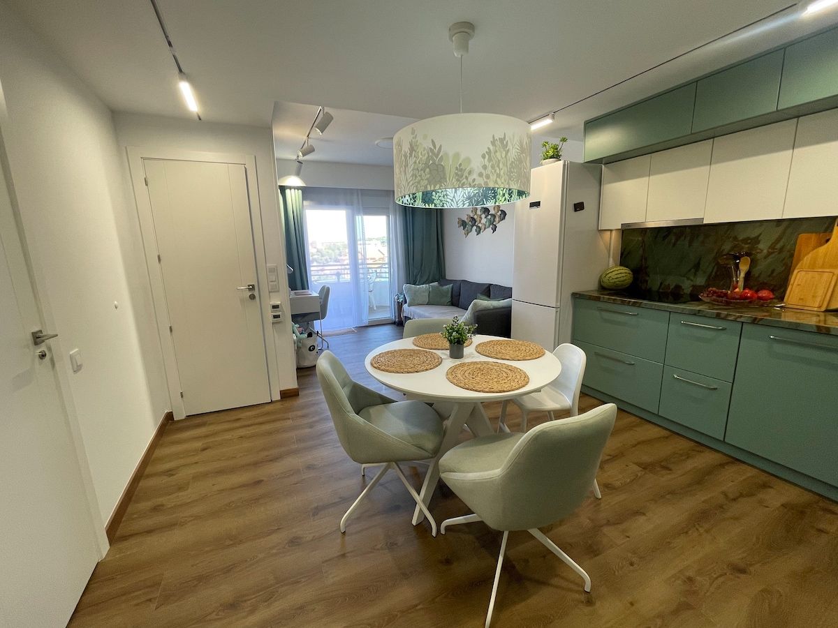 Open living room with round dining table and sage green kitchen
